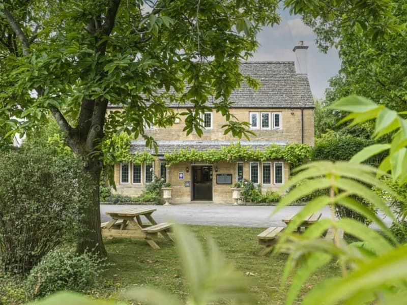 The Vines at Black Bourton, a stone Cotswold house seen through the trees